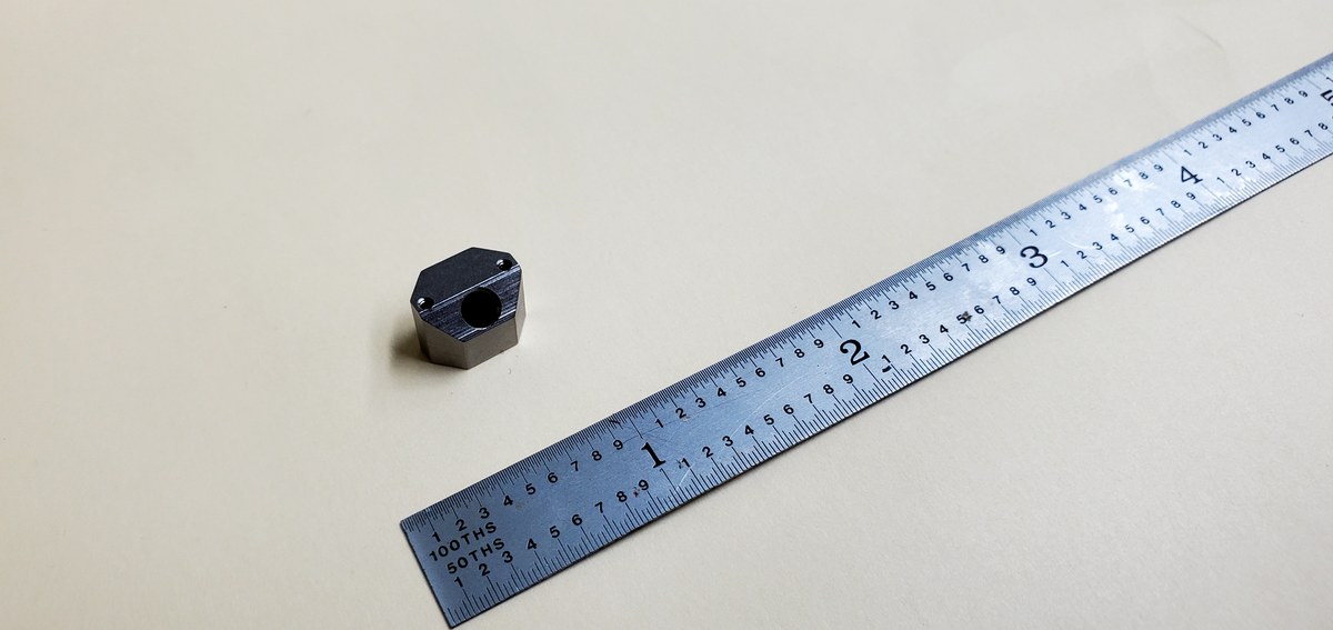 Small hex machined part next to ruler for scale